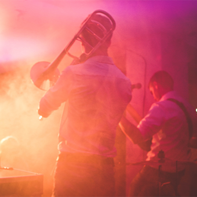 Trombone and guitar player performing in a pink/orange haze